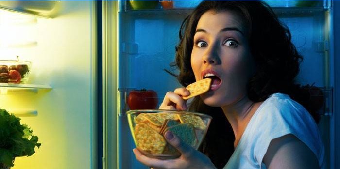 La ragazza davanti ad un frigorifero aperto mangia i cracker