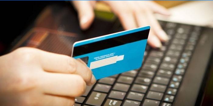 Ragazza di fronte a un computer portatile con una carta di credito in mano