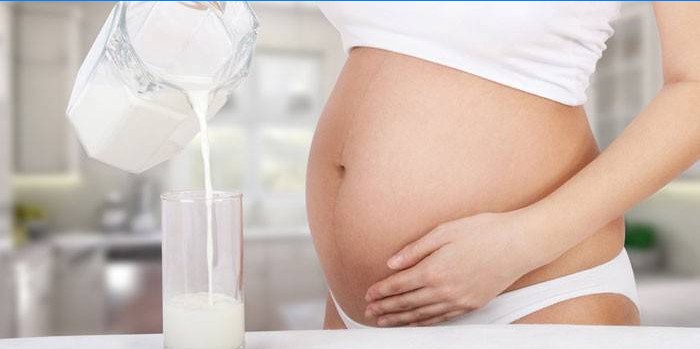 La donna incinta versa il latte al forno fermentato in un bicchiere